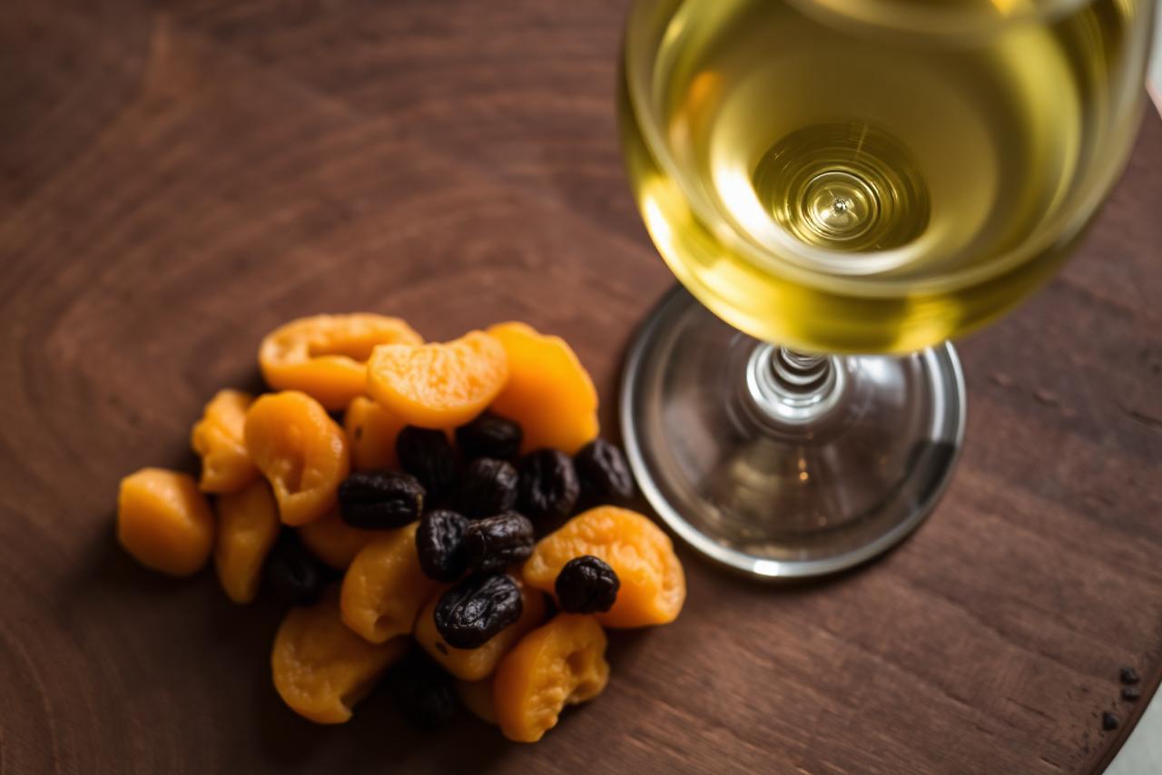 Bottles of wine and a bowl of dried apricots on a wooden surface.